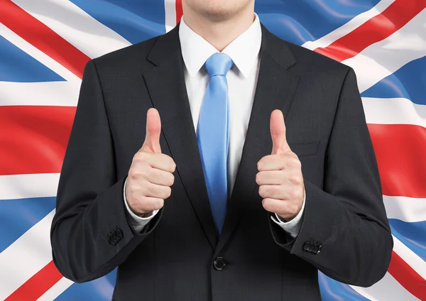 En person i en kostym tummen upp. Storbritannien flagga som bakgrund. — Stockfoto