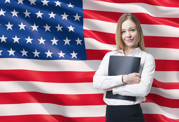 Hymyilevä bisnesnainen valkoisessa paidassa mustan kansion kanssa. Yhdysvaltain lippu taustana . — kuvapankkivalokuva