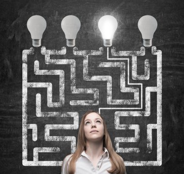 Beautiful woman is looking for the way how to solve the maze and reach the right light bulb as a concept of the perfect business solution.