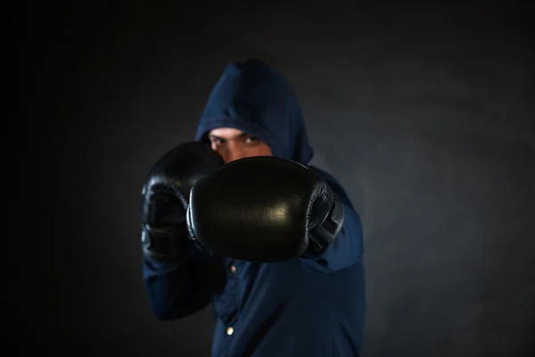 Человек в капюшоне в боевой позе в черных боксерских перчатках . — стоковое фото