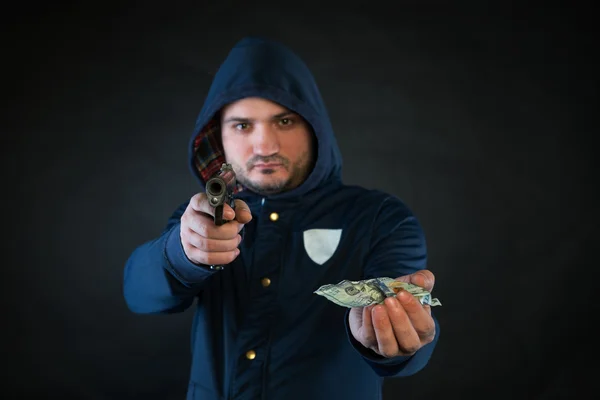 Una persona en una sudadera con capucha está apuntando y sosteniendo la otra mano con el billete de dólar. Un concepto del robo . —  Fotos de Stock