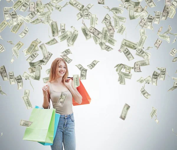 Eine fröhliche junge Frau mit den bunten Einkaufstüten aus den schicken Geschäften. Dollarnoten fallen von der Decke. Konkreter Hintergrund. — Stockfoto