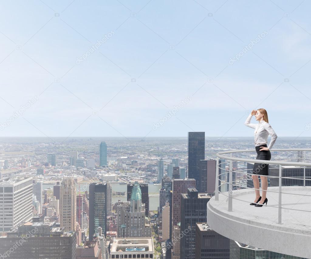 Business lady looks at the New York city standing on the top of the skyscraper terrace.