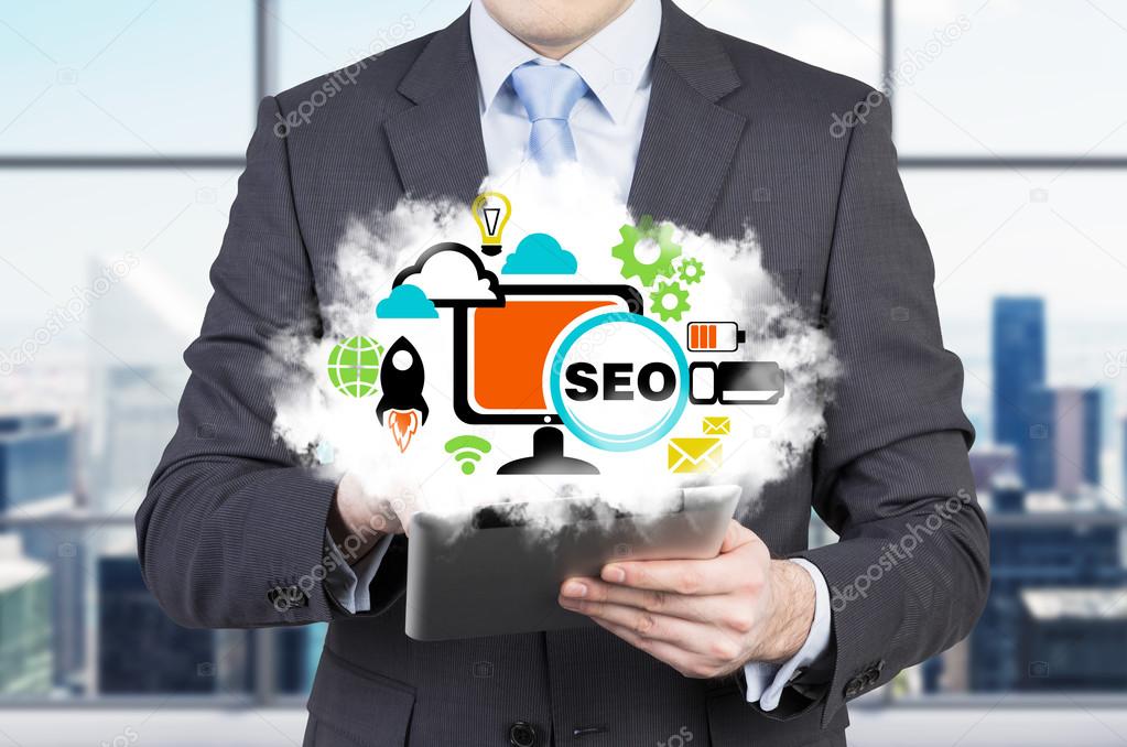 Businessman is holding a tablet with cloud projection and the acronym 'SEO'