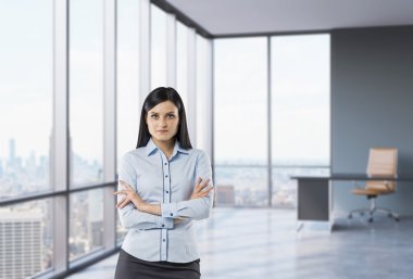 The brunette girl with crossed hands is standing in the corner panoramic office. New York view. clipart
