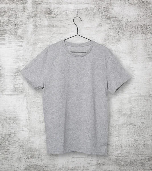 Close-up of the grey t-shirt on the clothes hanger. Concrete background. — Stock Photo, Image