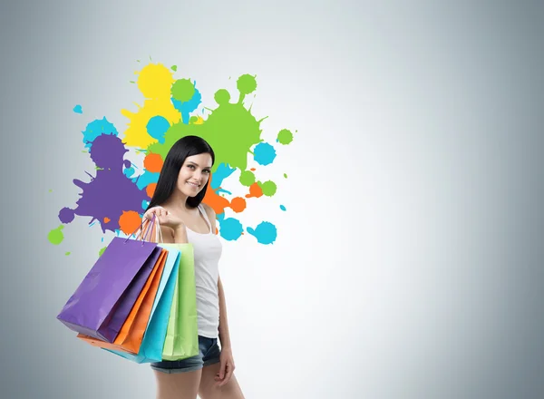 Красивая улыбающаяся молодая женщина с красочными сумками для покупок из модных магазинов. Студийный фон с нарисованными цветовыми пятнами магазинов . — стоковое фото