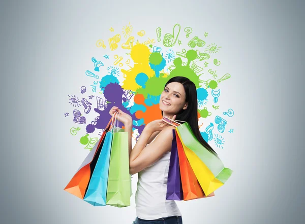 Beautiful smiling young woman with the colourful shopping bags from the fancy shops. Studio background with drawn shopping colorful spots. — Stock Photo, Image