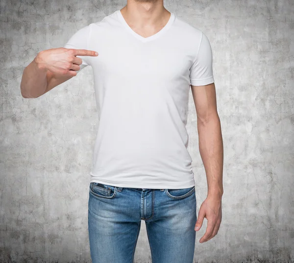 Primer plano de un hombre señalando con el dedo una camiseta en blanco. Fondo de hormigón . —  Fotos de Stock