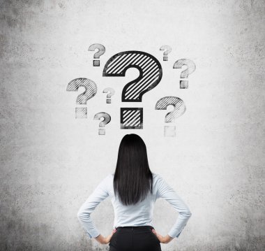 Rear view of the brunette who looks on the drawn question marks. Concrete background. clipart