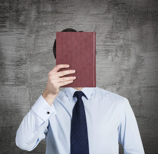 Una persona sostiene un libro rojo delante de la cabeza. Fondo de hormigón . —  Fotos de Stock
