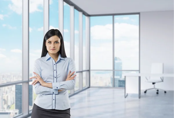 La ragazza bruna con le mani incrociate è in piedi nell'ufficio panoramico angolo. Vista di New York . — Foto Stock