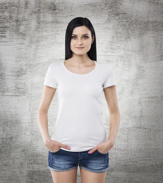 Brunette girl in a white t-shirt and denim shorts. Concrete background. — Stock Photo, Image