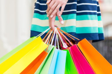 A lady in a skirt is holding a lot of colourful shopping bags.