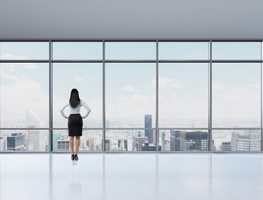 Rear view of brunette woman in the office who looks through the window. New York panoramic office. A concept of a successful woman in a business.