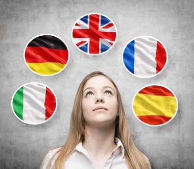 Beautiful lady is surrounded by bubbles with european countries' flags (Italian, German, Great Britain, French, Spanish). Learning of foreign languages concept. Concrete background.
