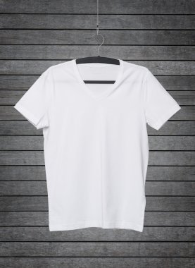 Close up of a V shape white t-shirt on cloth hanger. Dark concrete background.