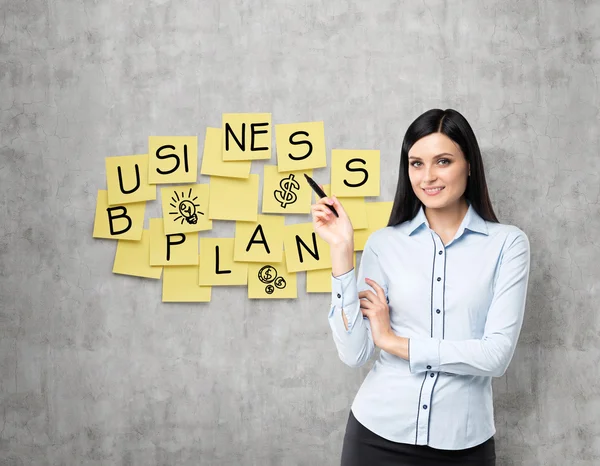 Brunette lade shows the new business plan. Yellow stickers are hanged on the concrete wall. — Stock Photo, Image