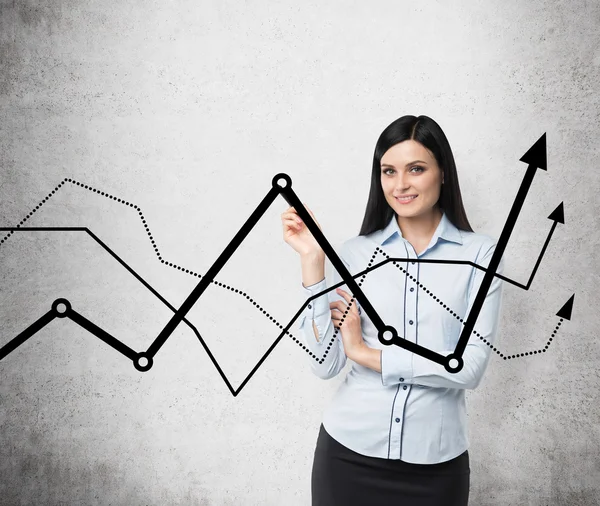 Brunette business lady presents a line graphs, which symbolise fluctuation of the business process. Concrete background. — Stockfoto