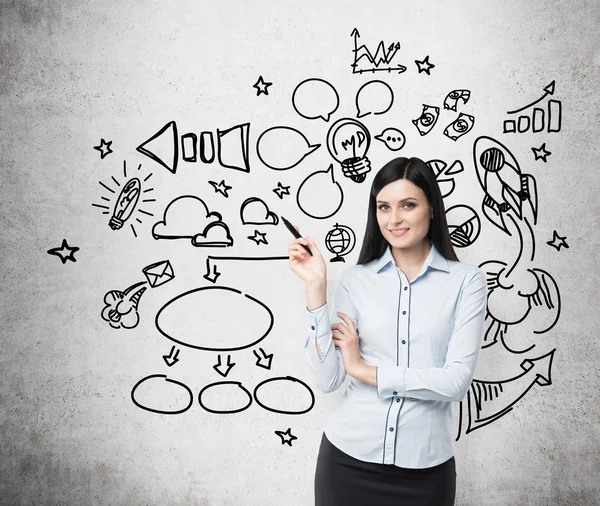 Young brunette business woman is thinking about optimisation of social media process. Chalk icons are drawn on the concrete wall. — Stockfoto