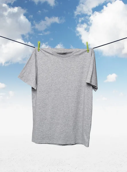 Primo piano di una t-shirt grigia sulla corda. Sfondo cielo nuvoloso . — Foto Stock