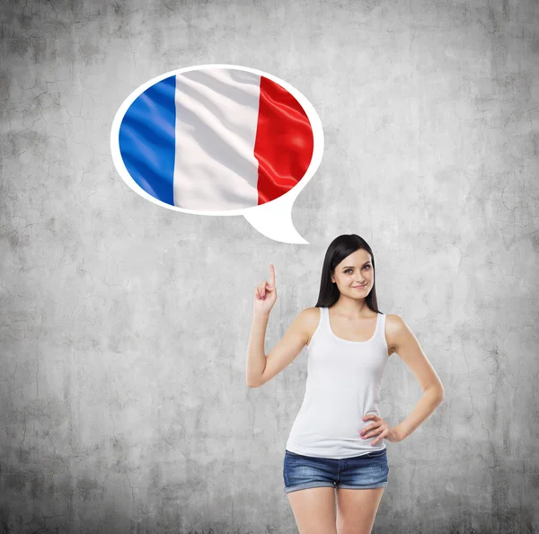 Brunette lady is pointing out the thought bubble with French flag inside. Concrete background. — 图库照片