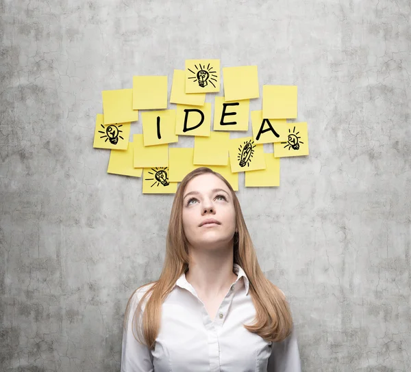 Jeune femme d'affaires est à la recherche de nouvelles idées d'affaires. Des autocollants jaunes avec le mot "idée" et des croquis de "ampoules" sont accrochés au mur en béton . — Photo