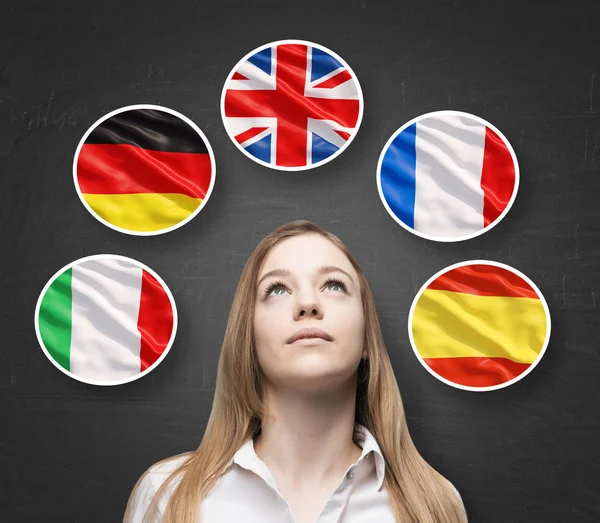 Beautiful lady is surrounded by bubbles with european countries' flags (Italian, German, Great Britain, French, Spanish). Learning of foreign languages concept. Blackboard background. — Stock Photo, Image