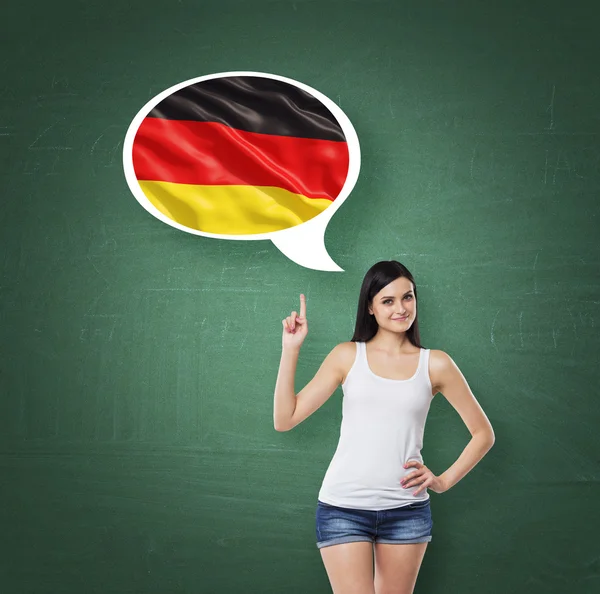 Beautiful woman is pointing out the thought bubble with German flag. Green chalk board background. — 图库照片
