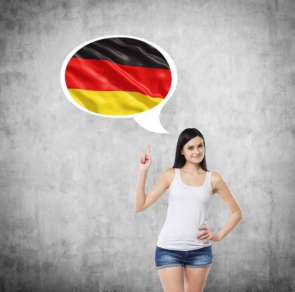 Brunette lady is pointing out the thought bubble with Germany flag inside. Concrete background. — Stock fotografie