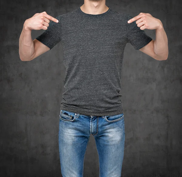 Um homem a apontar os dedos numa t-shirt cinzenta em branco. fundo de concreto escuro . — Fotografia de Stock