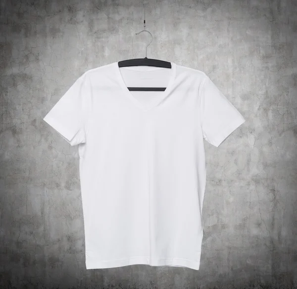 Close up of a V shape white t-shirt on cloth hanger. Concrete background. — 스톡 사진