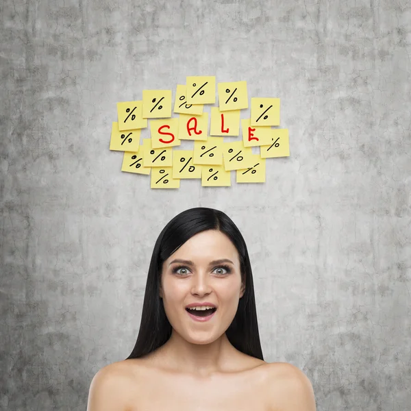 Portrait of an astonished brunette girl. Yellow stickers with the word ' sale ' are hanged on the concrete wall. — Stock Photo, Image