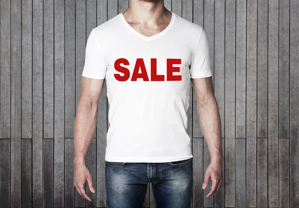 Close up of the body view of the man in a white t-shirt with the red word ' sale ' on the chest. Vertical wooden planks on the background. — 스톡 사진