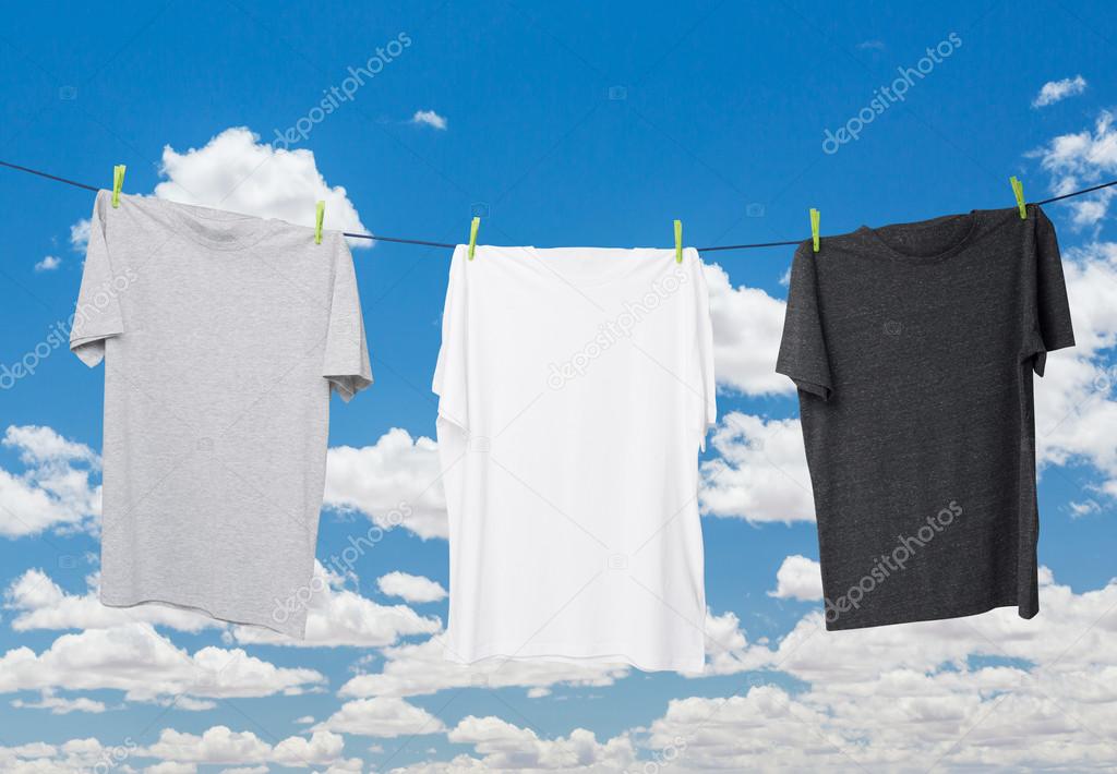 Close up of three t-shirts on the rope (grey, white and dark grey). Cloudy sky background.