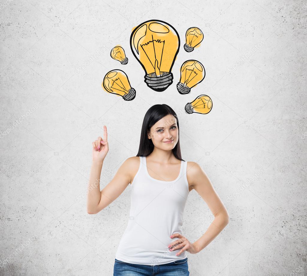 Brunette lady is pointing out the drawn yellow light bulbs. A concept of new ideas and creativity. Concrete background.