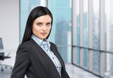 Portrait of a beautiful brunette lady in a formal suit. Panoramic business city view from the modern office.