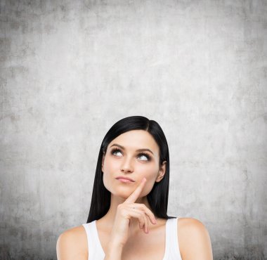 A portrait of a pensive brunette lady in a white tank top. Concrete background.