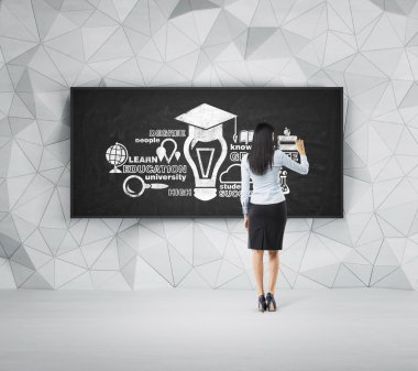 Rear view of full-length brunette student who is presenting educational concept on the black chalk board.