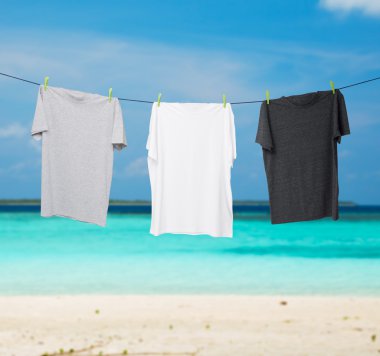 Close up of a dark grey, white and grey t-shirts on the rope. Tropical sand beach and ocean as background.