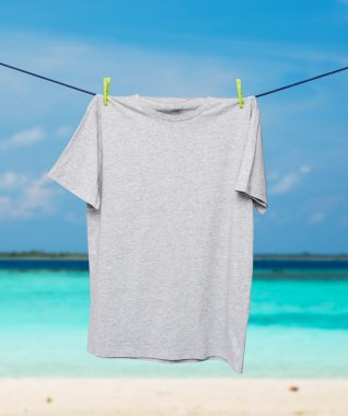 İp üzerinde gri bir t-shirt kapatın. Tropikal kum plaj ve okyanus arka plan olarak.