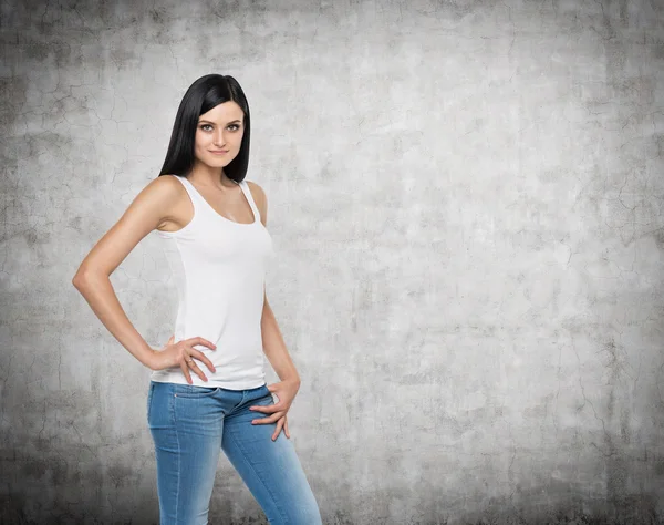 Close up of brunette girl in denims and white tank top. Concrete background. — Stock Photo, Image