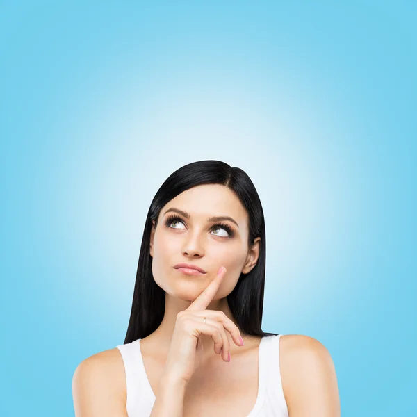 A portrait of a pensive brunette lady in a white tank top. Blue background. — Stockfoto