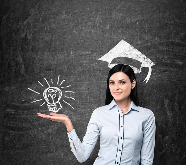 Brunette lady presents a light bulb as a concept of university degree. Graduation hat is drawn above her head. — ストック写真