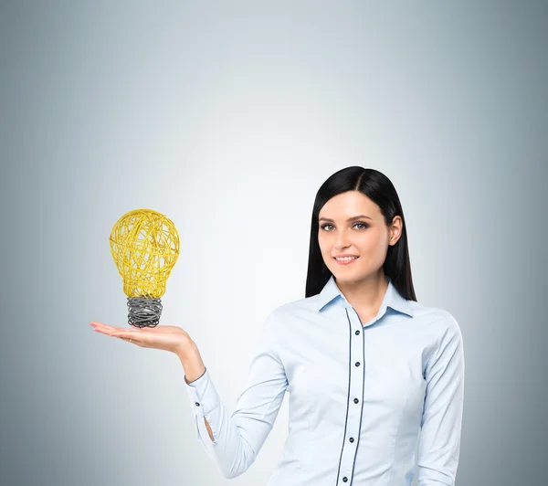 Brunette lady presents a light bulb as a concept of new idea in business. — стокове фото