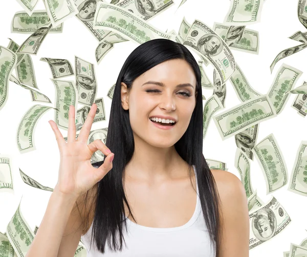 Brunette woman shows ok sign. Dollar notes are falling down over isolated background. — Zdjęcie stockowe