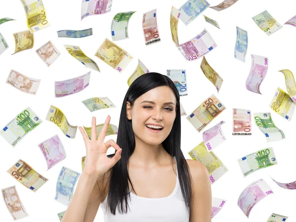 Brünette Frau zeigt ok Zeichen. Euro-Scheine fallen vor isoliertem Hintergrund. — Stockfoto