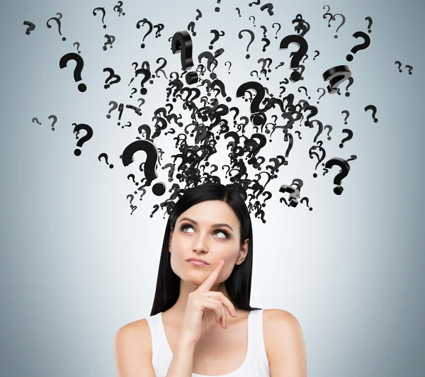 A portrait of a beautiful brunette with questioning expression and question marks above her head. — Stockfoto