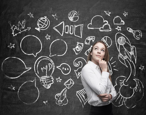 Young beautiful lady is thinking about optimisation of the marketing business process. Social media icons are drawn on the black chalk board. — Stockfoto