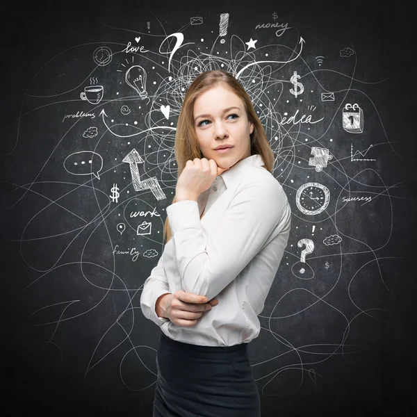 A portrait of a beautiful lady with questioning expression who is looking the best solution for the business problem. Chalk Business icons are drawn over the black chalkboard. — Stock fotografie